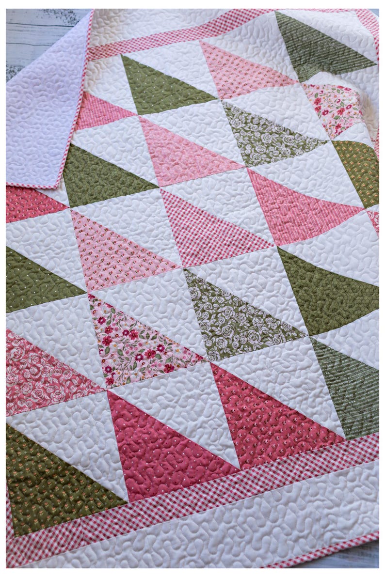 May include: A handmade quilt with a geometric pattern of triangles in shades of pink, green, and white. The quilt features various floral and patterned fabrics, with a red and white gingham border. The quilt is machine quilted.