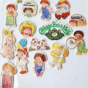 May include: A collection of Cabbage Patch Kids stickers featuring various characters, a butterfly, and text including Day Dreamer, Cry-Baby, smile, and Cabbage Patch Kids. The stickers depict children in colorful outfits, playing with toys, and animals.