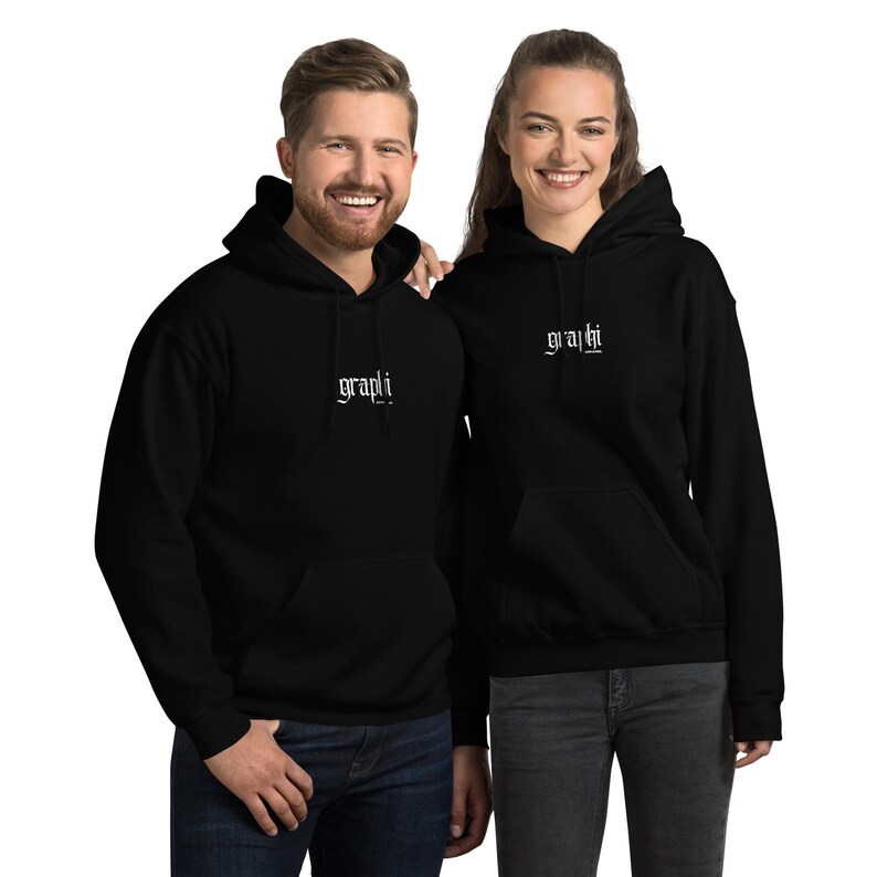 K&ouml;nnte beinhalten: Zwei schwarze Kapuzenpullover mit dem Wort "graphi" in wei&szlig;er Schrift. Die Sweatshirts haben eine Vordertasche und eine Kapuze mit Kordelzug. Die Personen tragen blaue Jeans. Der Hintergrund ist wei&szlig;.