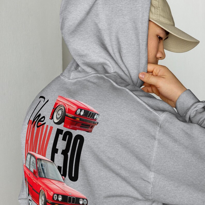 May include: A grey hoodie with a red car graphic and the text "The BMW E30". The design features two red car illustrations. The hoodie has a hood and a front pocket.