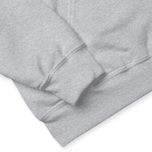May include: Close-up of a light grey hoodie. The image focuses on the sleeve and the lower portion of the hoodie, showcasing the ribbed cuff and the soft, textured fabric. The hoodie appears to be made of a comfortable material.
