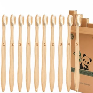 以下が含まれることがあります： 白い毛の付いた1から5までの番号が振られた10本の竹製歯ブラシのセット。歯ブラシは一列に並んでいます。背景には、パンダのイラストと「Bamboo Toothbrush」の文字が入った段ボール箱があります。