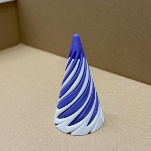 以下が含まれることがあります： 紫色の先端と、白と紫のストライプが交互に並んだスパイラルデザインが特徴の、3Dプリントされた円錐形オブジェクト。ベースは白で、テクスチャ加工された曲線模様があります。ニュートラルな色調の表面に置かれています。