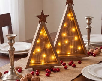 Puede incluir: Dos decoraciones triangulares de árbol de Navidad de madera con un acabado marrón natural, cada una rematada con una estrella de metal oscuro. Los centros huecos están iluminados por finas tiras de luces LED de color blanco cálido.