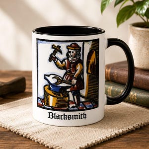 Puede incluir: Una taza de cerámica blanca con asa e interior negros, que presenta una ilustración colorida de un herrero trabajando en un yunque con un martillo. La palabra Blacksmith está impresa en una fuente gótica negra en la base del diseño.