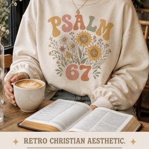 May include: A cream-coloured sweatshirt featuring the word "PSALM" in retro lettering, a floral design, and the number "67". The design is part of a retro Christian aesthetic theme.