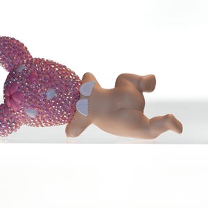 K&ouml;nnte beinhalten: Eine rosa Hasenfigur mit kristallartiger Textur auf Kopf und Ohren, gepaart mit einer hellh&auml;utigen Babyfigur. Der Hase liegt auf der Seite, die Babyfigur ist davor positioniert.