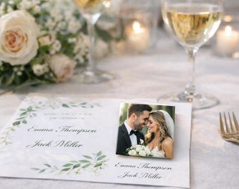 May include: A wedding reception table setting featuring a square photo of a couple, a wedding invitation, and a glass of champagne. The invitation is white with green floral accents and the names "Emma Thompson" and "Jack Miller".