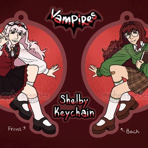 May include: A double-sided Shelby keychain featuring a cartoon vampire character. The front shows a character in a red and black outfit, while the back depicts a character in a green sweater and plaid skirt. The keychain is 8.89 cm in height.