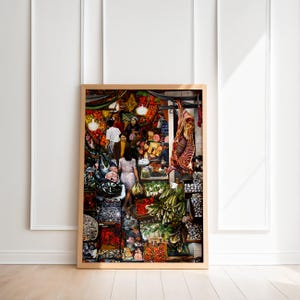 May include: Framed art print depicting a bustling marketplace scene. The artwork showcases a variety of fresh produce, meats, and people. The color palette includes vibrant reds, greens, and yellows, creating a lively and engaging composition.