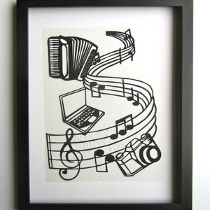 May include: Black and white paper cut-out art framed in a black frame. The art features a musical staff with notes, a treble clef, a laptop, a camera, and an accordion. The text "Dear Ziv Happy 40th" is included in the art.
