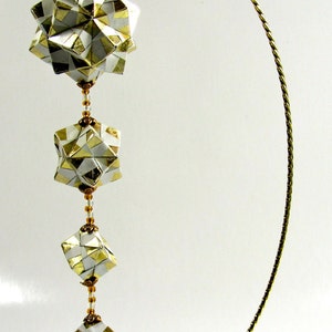 May include: A gold-colored metal stand with a twisted wire design holds a string of four origami paper balls. The balls are white with gold accents and are connected by a string of beads. A small origami crane hangs from the bottom of the string.