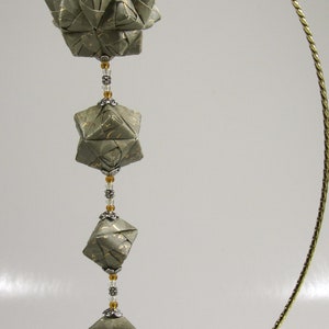 May include: A gold metal stand with a chain of origami paper stars and beads hanging from it. The stars are a light green color with gold accents.