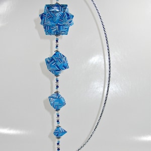 May include: A blue and white origami ornament hanging from a silver stand. The ornament is made of paper and has a geometric design. It is a unique and beautiful decoration for any home.