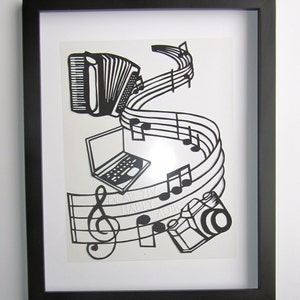May include: Black and white paper cut art framed in a black frame. The art features a musical staff with notes, a camera, a laptop, and an accordion. The text "Dear Ziv Happy 40th" is visible on the staff.