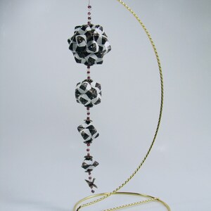 May include: A set of four origami paper balls, each with a black and white geometric pattern, are strung together with purple beads and hung from a gold metal stand.