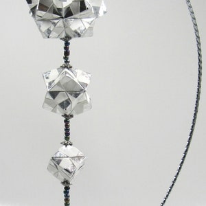 May include: A silver origami mobile with four star-shaped pieces hanging from a silver wire stand. The mobile is decorated with iridescent beads.