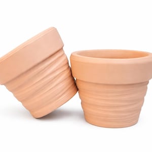 Könnte beinhalten: Zwei Blumentöpfe aus Terrakotta. Ein Topf steht aufrecht, der andere ist geneigt und lehnt am ersten. Beide Töpfe haben ein geriffeltes, strukturiertes Design auf der Außenseite und einen glatten Rand. Diese Töpfe eignen sich zum Pflanzen von Blumen oder Kräutern.