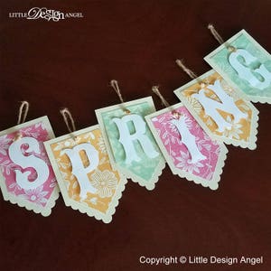 May include: A spring banner with the word "SPRING" spelled out in white letters on colorful pennants with floral patterns. The pennants are strung together with twine.