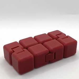 May include: A red fidget cube toy made up of eight connected, square blocks. Each block has a slightly textured surface and is linked to its neighbours by a small, rectangular hinge. The toy is designed for manipulation and play.