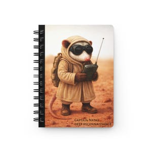 May include: Spiral-bound notebook featuring an illustration of a possum in a tan coat, goggles, and a backpack, holding a radio. The text "CAPTAIN NATAS DEEP RECONNAISSANCE" is printed at the bottom. The background is a desert landscape.