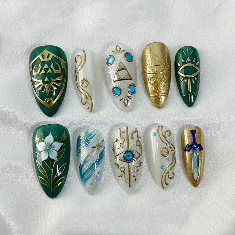 May include: A set of ten artificial nails with various designs. The nails feature gold and green shield, eye, and sword designs, along with floral and abstract patterns. Some nails have a white base with gold accents and blue gems.