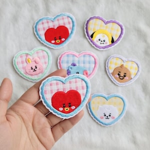 May include: A collection of heart-shaped embroidered patches featuring cartoon characters. Each patch has a gingham pattern background and a colorful border. The patches are in various colors, including red, yellow, pink, and blue.