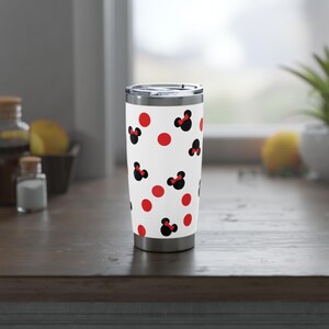 May include: A white travel tumbler with a silver lid, adorned with a pattern of red polka dots and black Minnie Mouse silhouettes with red bows. The tumbler is stainless steel and appears to be insulated.
