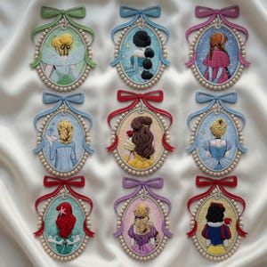 May include: Nine embroidered oval portraits of animated characters, each with a different hairstyle and dress, are displayed. Each portrait is framed with a pearl-like border and a ribbon bow at the top. The characters are in various colors, including blue, red, and yellow.