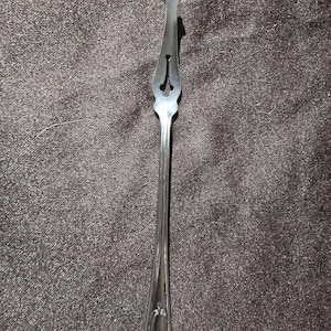 May include: A silver-colored, pointed serving utensil with a decorative handle. The utensil has a long, slender handle and a pointed tip with a decorative cutout. The handle has a slight curve and a decorative pattern near the base.