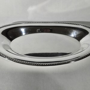 May include: A shiny, oval-shaped silver serving tray. The tray has a smooth, reflective surface and a decorative beaded edge. The tray is designed for serving food or displaying items.