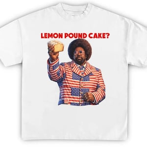 Puede incluir: Camiseta blanca con un gráfico de una persona sosteniendo un trozo de bizcocho de limón. La persona lleva un traje rojo, blanco y azul. El texto "LEMON POUND CAKE?" está impreso en rojo encima del gráfico.