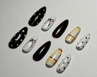 May include: A collection of ten almond-shaped artificial nails. Designs include black with white polka dots, white with a burgundy bow, solid burgundy, yellow with a brown plaid pattern, and white with black polka dots.