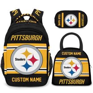 May include: A black and yellow Pittsburgh Steelers backpack, pencil case, and lunch bag set. Each item features the Steelers logo, the word "Pittsburgh", and space for a custom name. The backpack has black mesh side pockets.