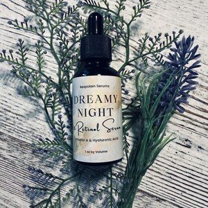 May include: A black glass bottle of Dreamy Night Retinol Serum, 1 oz by volume, with a dropper, set against a backdrop of lavender and greenery. The label reads "Bespoken Serums" and lists Vitamin A & Hyaluronic Acid.