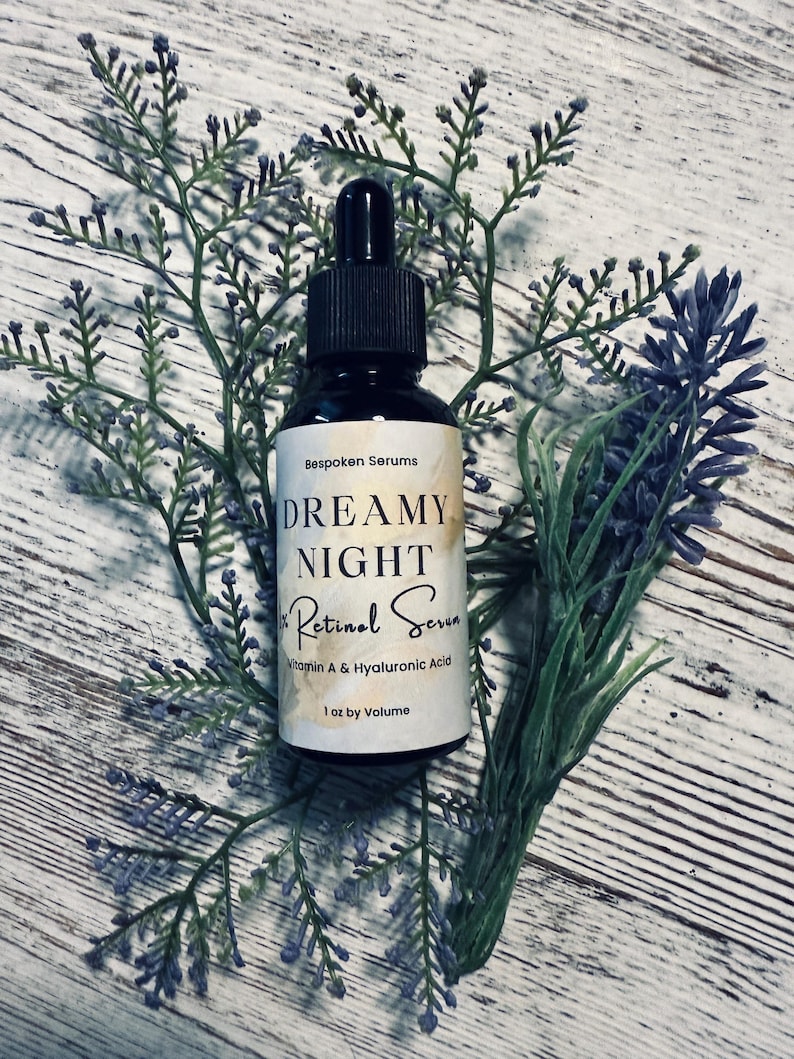 May include: A black glass bottle of Dreamy Night Retinol Serum, 1 oz by volume, with a dropper, set against a backdrop of lavender and greenery. The label reads "Bespoken Serums" and lists Vitamin A & Hyaluronic Acid.