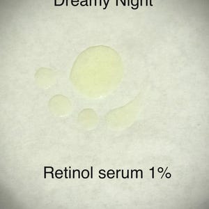 May include: A close-up of a light-colored liquid serum with the text "Dreamy Night" and "Retinol serum 1%" in black. The serum is in several small droplets on a white surface.
