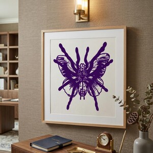 Può includere: Una stampa incorniciata con un design ibrido tarantola-farfalla viola. L'opera d'arte è ambientata su uno sfondo color crema all'interno di una cornice in legno chiaro. La stampa è montata su una parete sopra una scrivania in legno con un taccuino e un orologio.