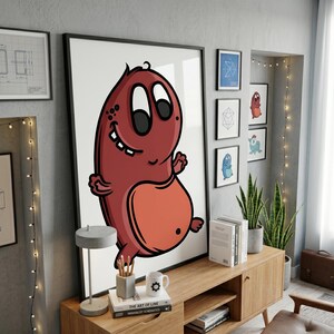 May include: A large framed wall art print featuring a cartoonish, maroon-colored creature with a light orange belly, large white eyes, and a wide grin. The character has a rounded body, small limbs, and is set against a plain white background.