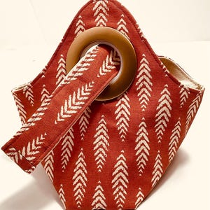 May include: A red tote bag with a white arrow pattern. The bag has a wooden handle and a matching strap that goes through the handle. The interior of the bag is a light beige color.
