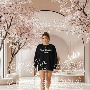 Puede incluir: Una sudadera negra de manga larga con el texto "Your Design Here" en blanco. La persona lleva zapatillas y calcetines blancos. El fondo presenta cerezos en flor y un interior moderno.