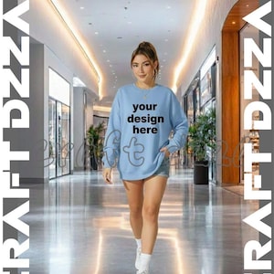 Puede incluir: Una persona lleva una sudadera azul claro con el texto "your design here" en un centro comercial. La sudadera tiene cuello redondo y mangas largas. La persona lleva pantalones cortos de mezclilla, calcetines blancos y zapatillas blancas. El fondo es un centro comercial moderno.