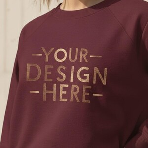 Puede incluir: Sudadera burdeos con mangas raglán. El texto dorado "-YOUR DESIGN-HERE-" está en la parte delantera. Esta sudadera informal está hecha de un material suave, adecuada para el uso diario.