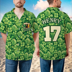 May include: Green button-down shirt with a shamrock and leaf pattern. The front features a beer graphic with the word "Slainte". The back displays the name "Henry" and the number "17" in a bold font. The shirt is worn with blue jeans.