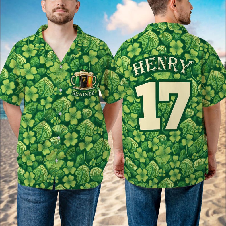May include: Green button-down shirt with a shamrock and leaf pattern. The front features a beer graphic with the word "Slainte". The back displays the name "Henry" and the number "17" in a bold font. The shirt is worn with blue jeans.