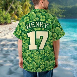 May include: Green button-up shirt with a pattern of shamrocks and leaves. The shirt has the name "HENRY" and the number "17" on the back in a cream color. The shirt is short-sleeved.