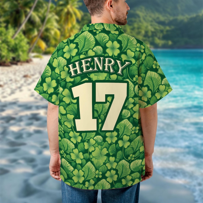 May include: Green button-up shirt with a pattern of shamrocks and leaves. The shirt has the name "HENRY" and the number "17" on the back in a cream color. The shirt is short-sleeved.