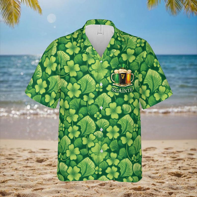 May include: Green short-sleeved shirt with a pattern of shamrocks and leaves. The shirt features a collar and buttons. A graphic of three beer mugs with the word "Sl&aacute;inte" is on the front.