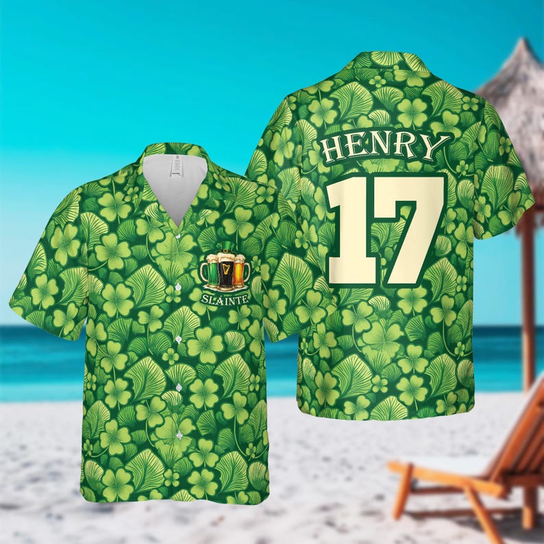 May include: Green short-sleeved shirt with a pattern of shamrocks and leaves. The shirt has a V-neck and features the name "HENRY" and the number "17" on the back. The front of the shirt has a graphic of beer mugs and the word "Slainte".