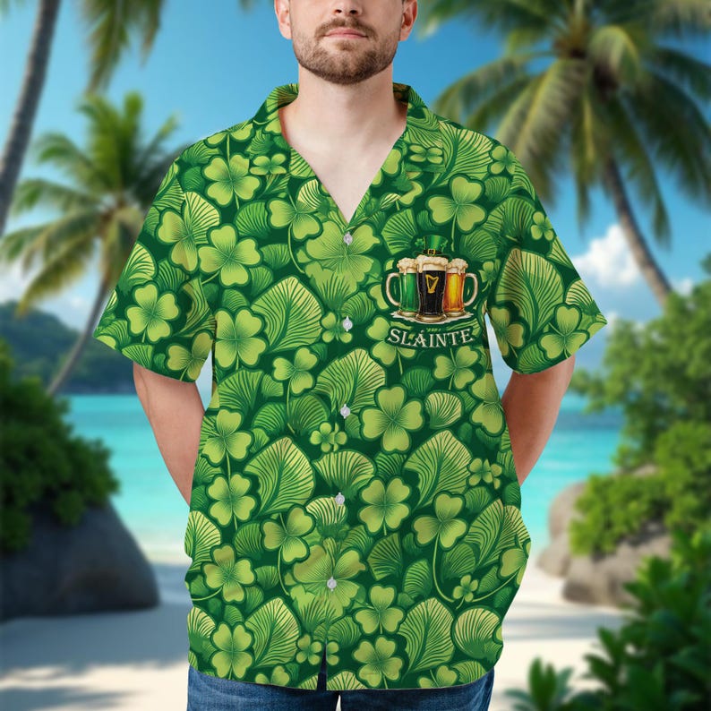 May include: Green button-up shirt with a shamrock and leaf pattern. The shirt features a design of three beer mugs with the word "SL&Aacute;INTE" below. The background shows a beach scene with palm trees and blue water.